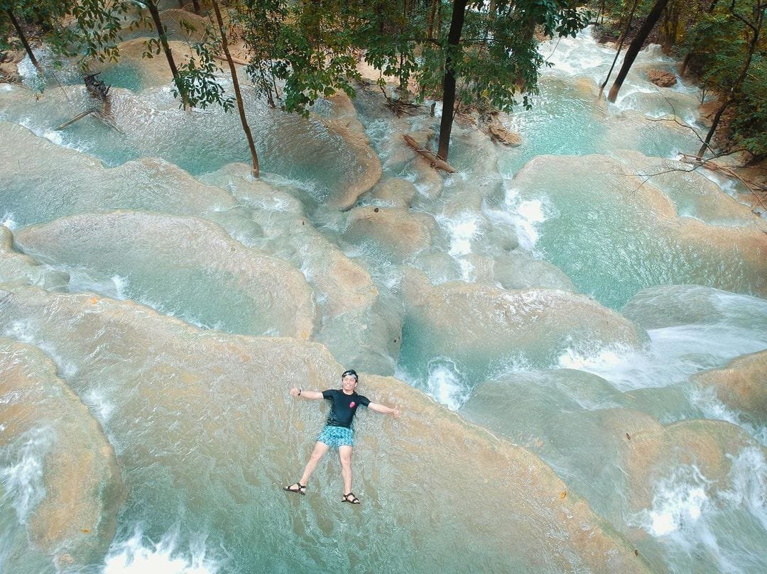 Visitors wading in the natural tiered pools of Kaparkan Falls surrounded by white limestone formations