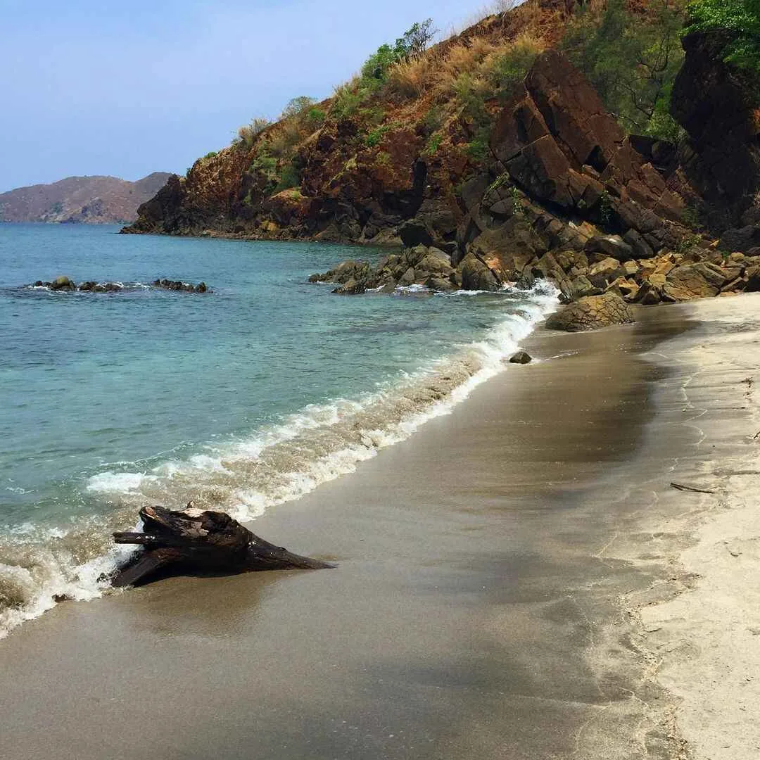 Wide gray sand beach at Nagsasa Cove with calm shallow water and forested hills in the background