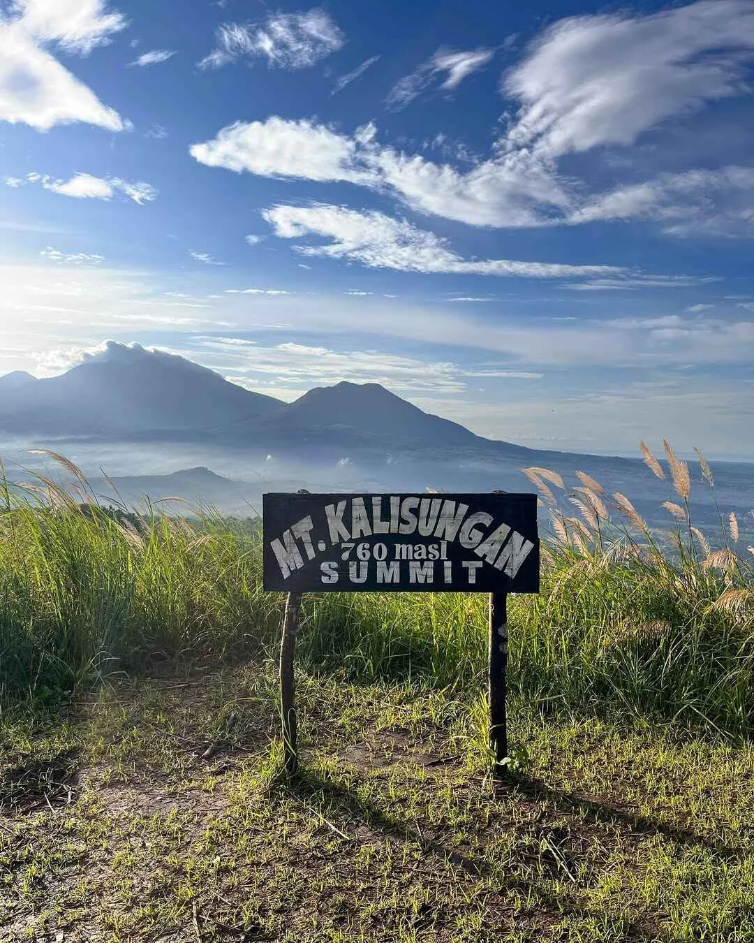 White summit cross on Mt. Kalisungan's open grassland peak with panoramic Laguna countryside views