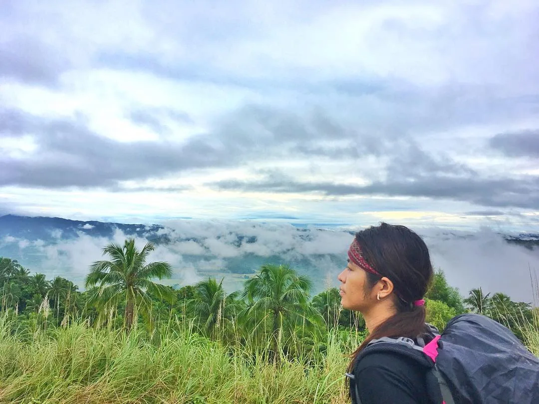 Open grassy campsite plateau near Buruwisan Falls on Mt. Romelo, surrounded by tall trees and morning mist