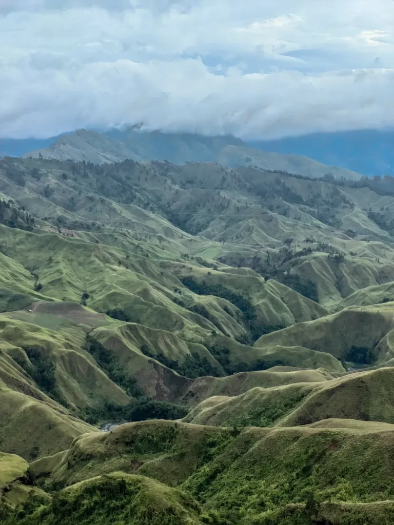Close-up landscape of Bukidnon’s grassy ridges near Panimahawa Ridge with thick cloud cover hanging over distant mountains.