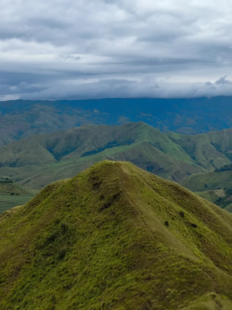Narrow grassy spine on Panimahawa Ridge with surrounding green mountains in Bukidnon beneath heavy rain clouds.