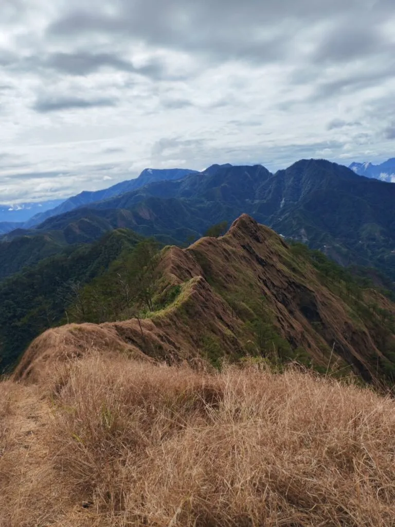 Hiker standing at the exposed summit ridge of Mt. Kimat Patil-Ao in Cervantes, Ilocos Sur, with sweeping Cordillera views