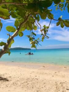 Fine white sand at Gumasa Beach with gentle waves washing the shore and beachgoers relaxing under natural tree shade