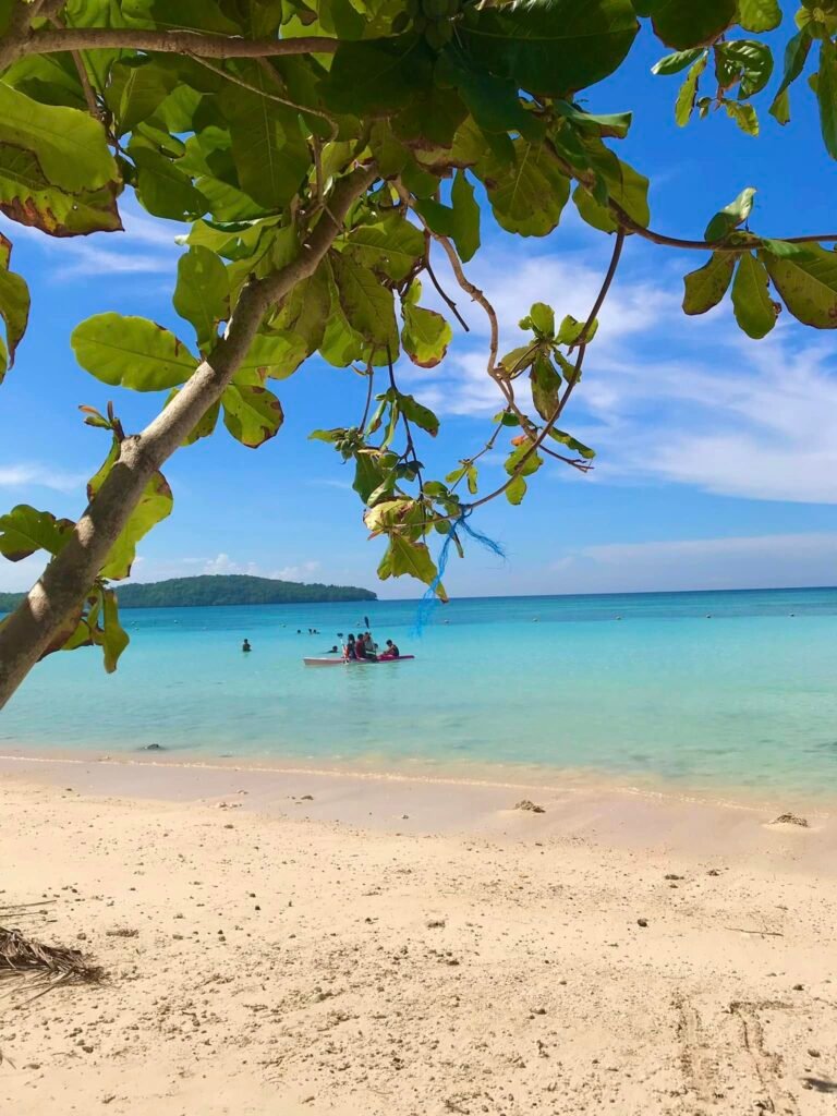 Fine white sand at Gumasa Beach with gentle waves washing the shore and beachgoers relaxing under natural tree shade