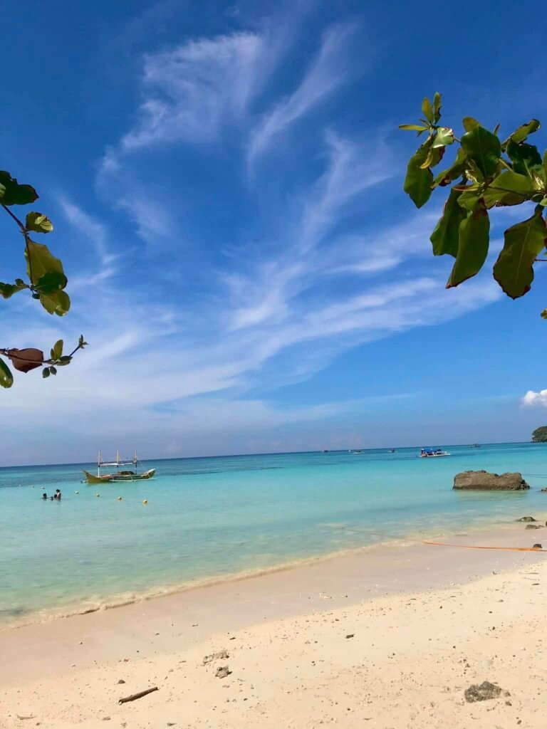 Fine white sand at Gumasa Beach with gentle waves washing the shore and beachgoers relaxing under natural tree shade
