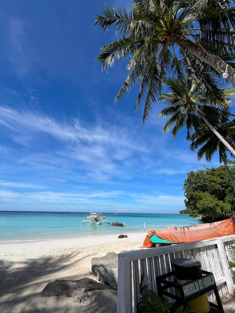 View from a motorized banca boat approaching the Gumasa Beach coastline with resort structures and palm trees in the background