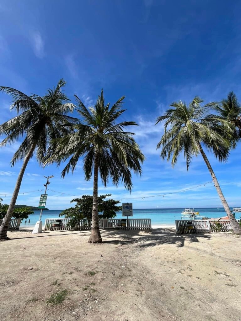 Wide view of Gumasa Beach's white sand shoreline along the Celebes Sea in Sarangani, Philippines, with calm blue water and resort structures visible