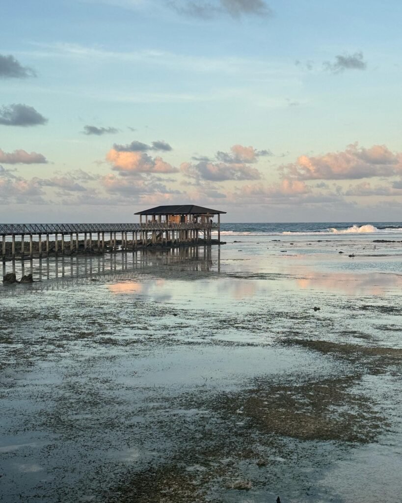 Wooden boardwalk extending over the reef at Cloud 9 Siargao with waves breaking below and blue sky overhead