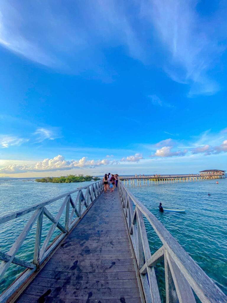 Wooden boardwalk extending over the reef at Cloud 9 Siargao with waves breaking below and blue sky overhead