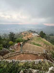 Hiker standing on Mt. Yangbew grassy summit with panoramic view of La Trinidad valley and Baguio City in the background