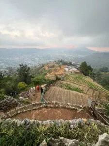 Hiker standing on Mt. Yangbew grassy summit with panoramic view of La Trinidad valley and Baguio City in the background