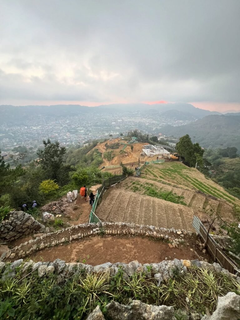 Hiker standing on Mt. Yangbew grassy summit with panoramic view of La Trinidad valley and Baguio City in the background
