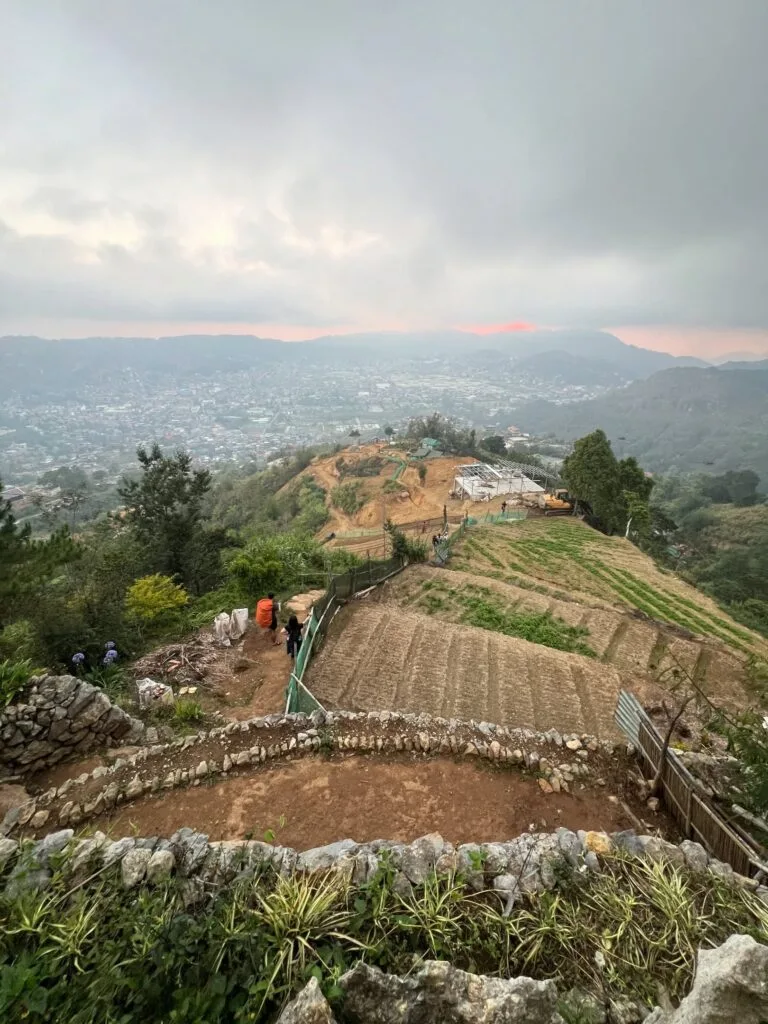 Hiker standing on Mt. Yangbew grassy summit with panoramic view of La Trinidad valley and Baguio City in the background