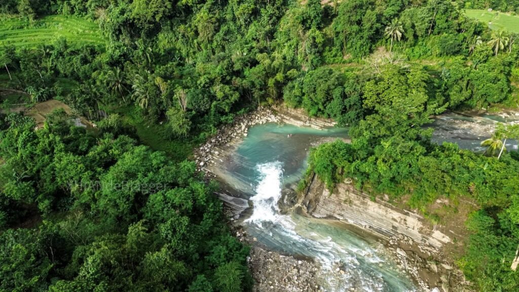 Natural plunge pool at the base of Kintukudan Falls with swimmers and sheer rock walls overhead